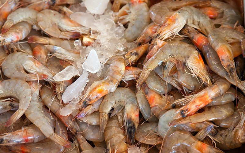 Fresh raw prawns displayed on ice at a market.