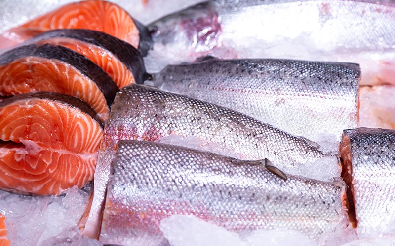 Fresh salmon steaks and whole fish displayed on ice.