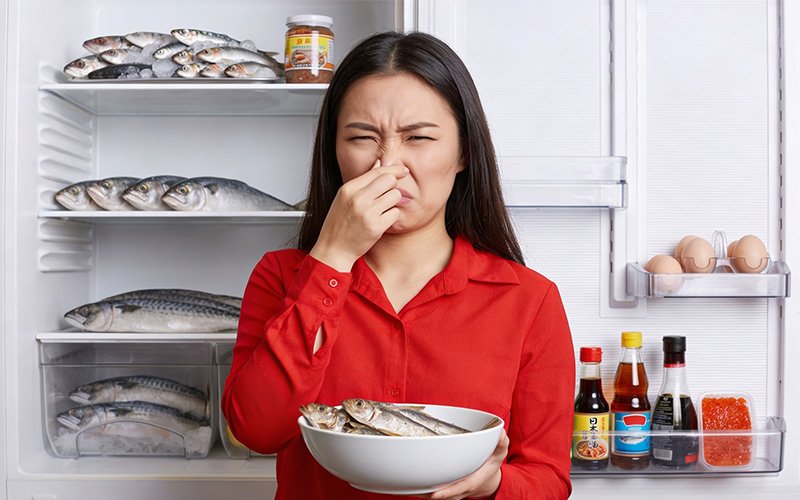Woman pinching her nose from fishy smell in kitchen.