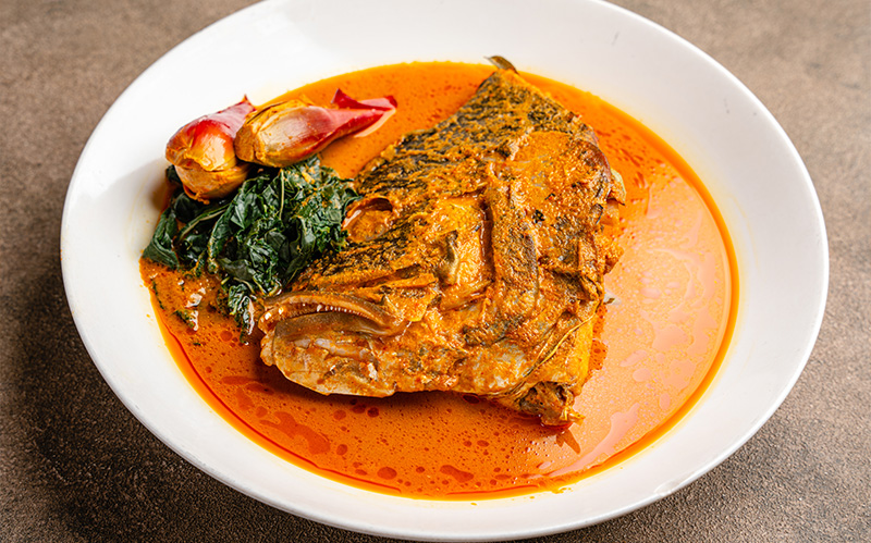 singapore-style-fish-head-curry-served-in-a-white-bowl-with-greens-and-ginger-bud